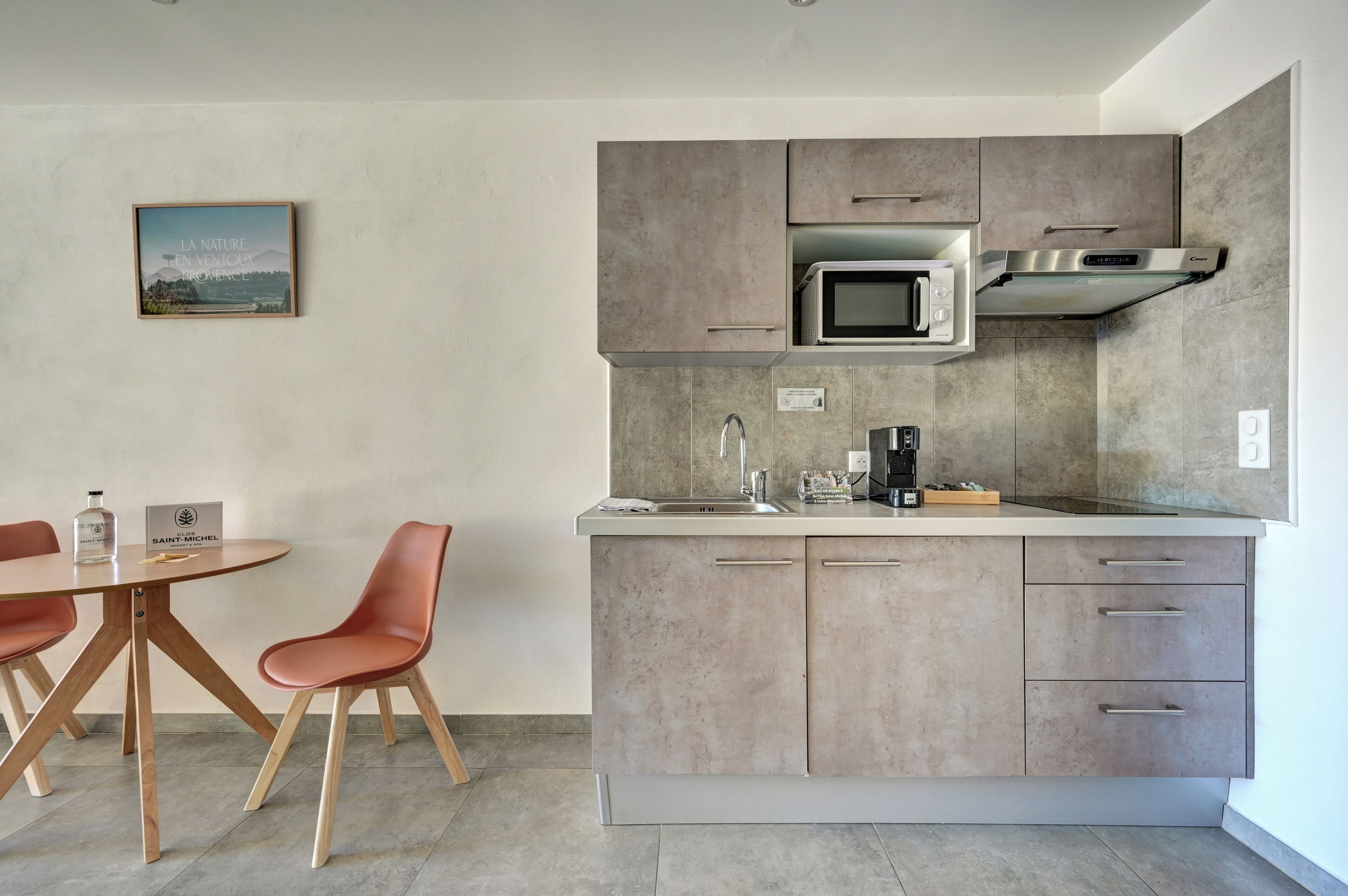 Een moderne keuken met een ingebouwde magnetron, een roestvrijstalen afzuigkap en een spoelbak. Er staat een eettafel met twee stoelen en een klein kookeiland met een spoelbak.