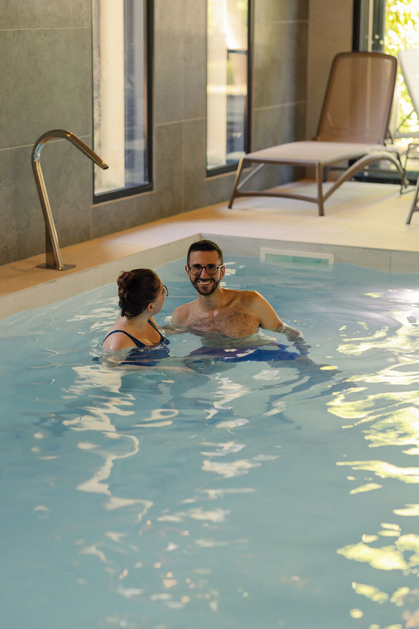 En inomhuspool med fri sikt över poolens kant, ett metallräcke och en solstol i bakgrunden.