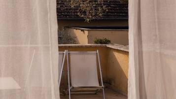 Un balcón con una silla plegable de metal, piso de baldosas y un edificio con techo de tejas al fondo.