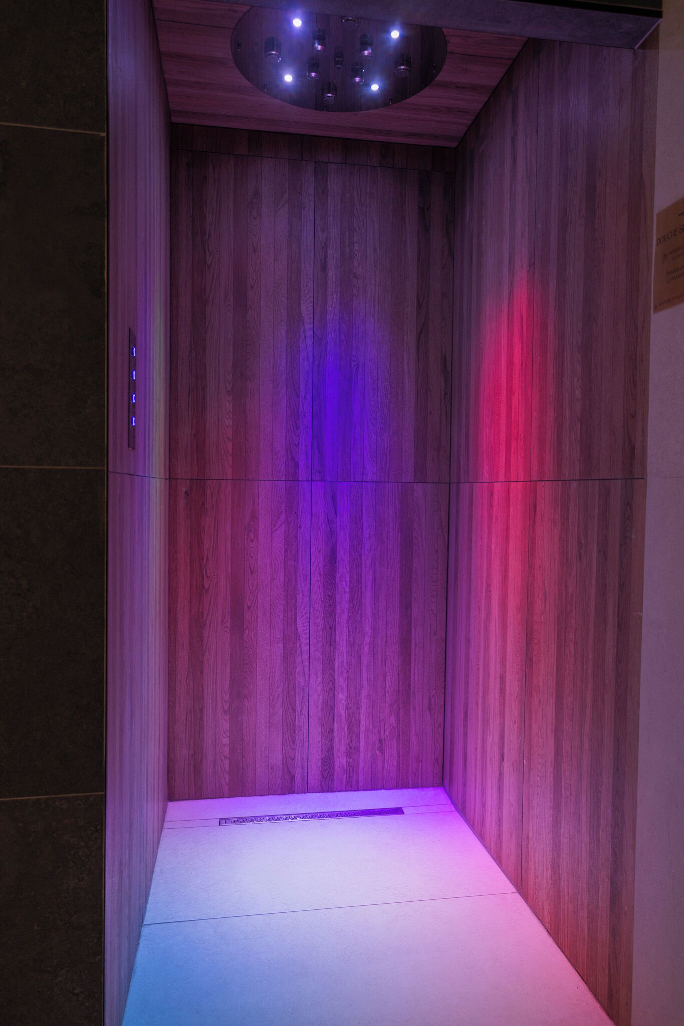 A wooden-paneled room with a ceiling light fixture and a strip of LED lighting on the floor.