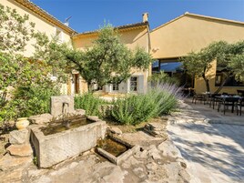 Un patio con una fuente de piedra, mobiliario exterior y un edificio de fachada amarilla.