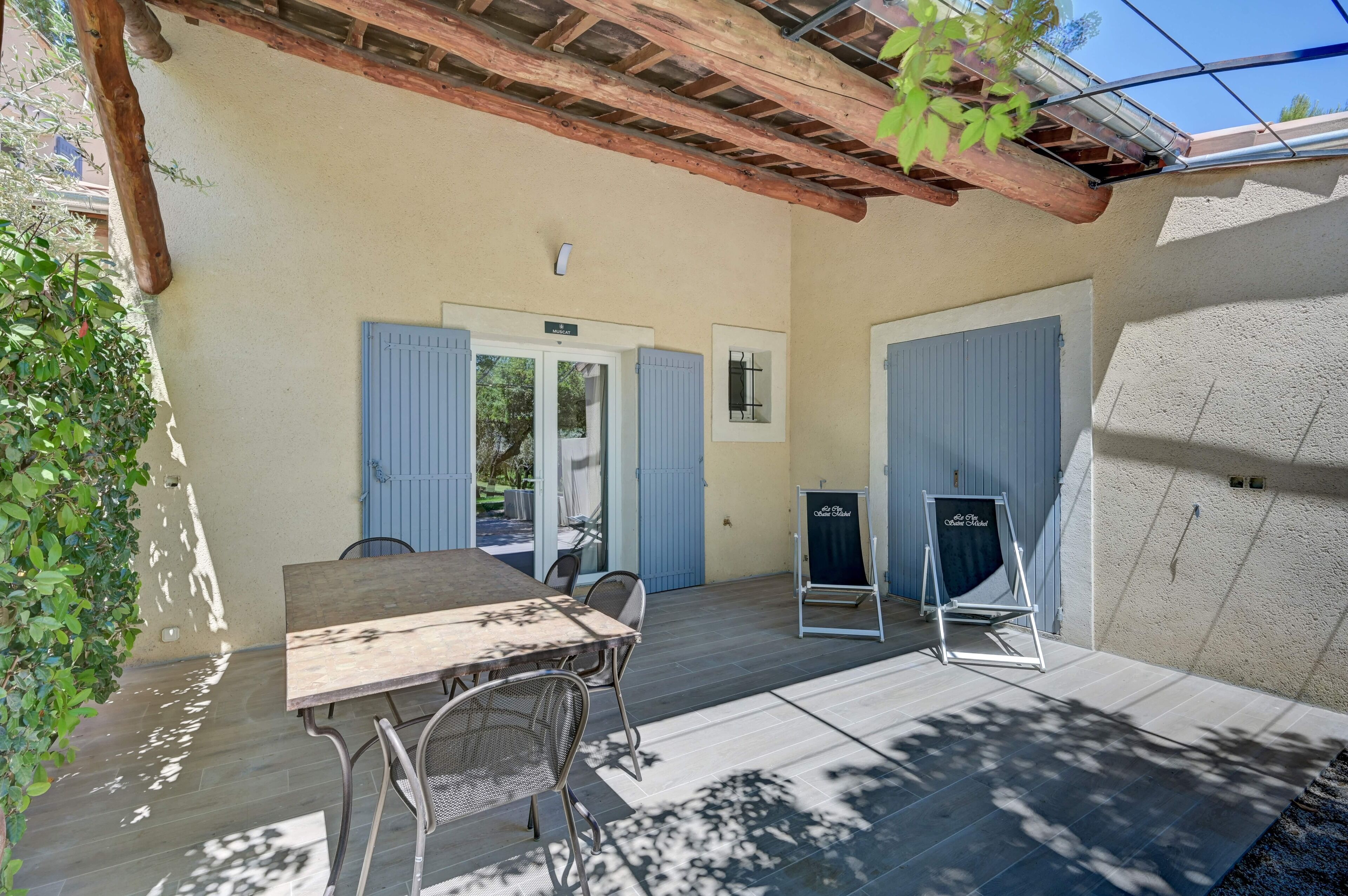 An outdoor patio area with a wooden table and chairs, a pergola overhead, and a view of the street.