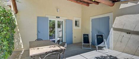 An outdoor patio area with a wooden table and chairs, a pergola overhead, and a view of the street.