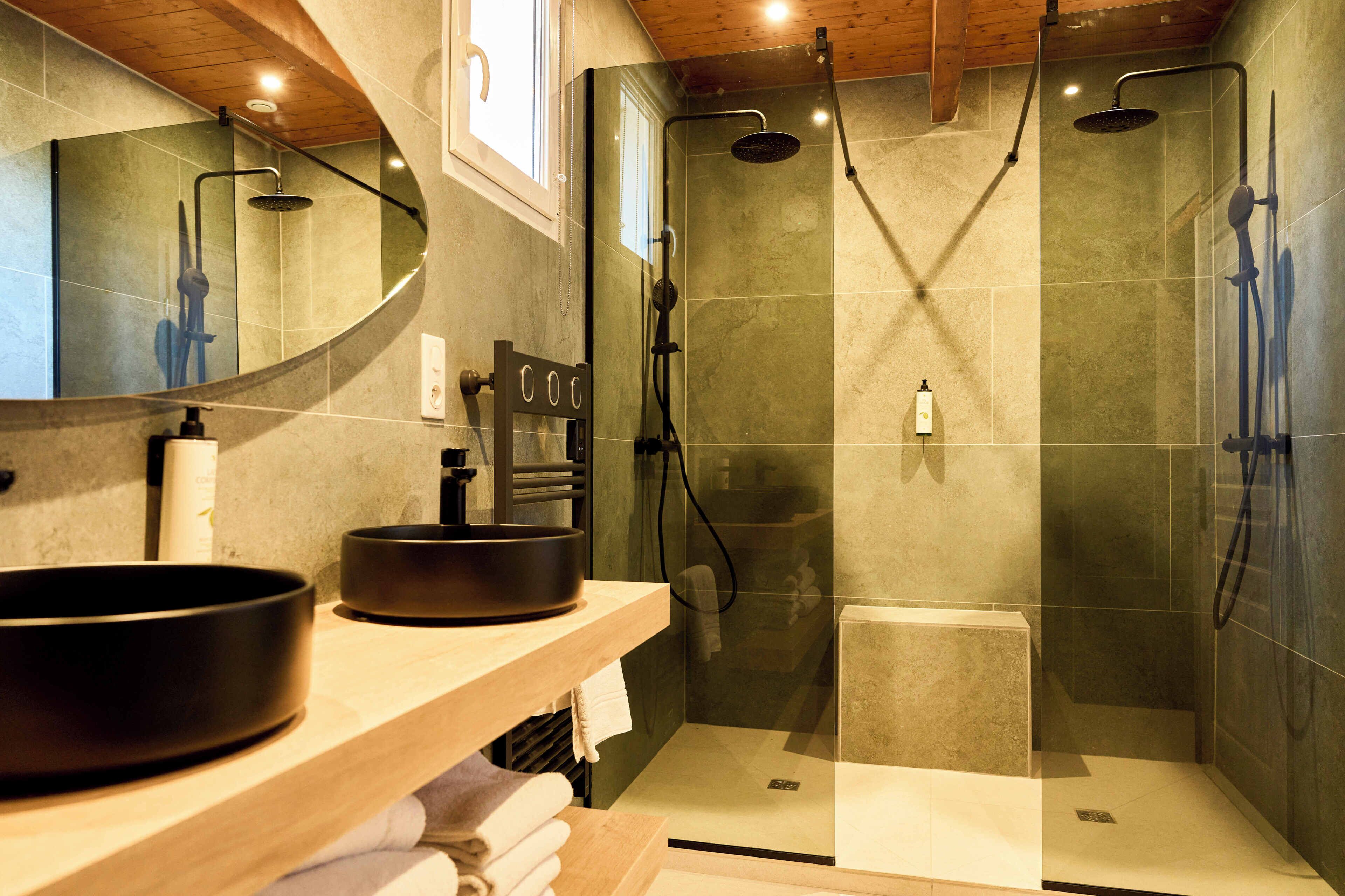 Une salle de bain moderne avec un grand miroir, un lavabo rond et une douche séparée par une paroi de verre.
