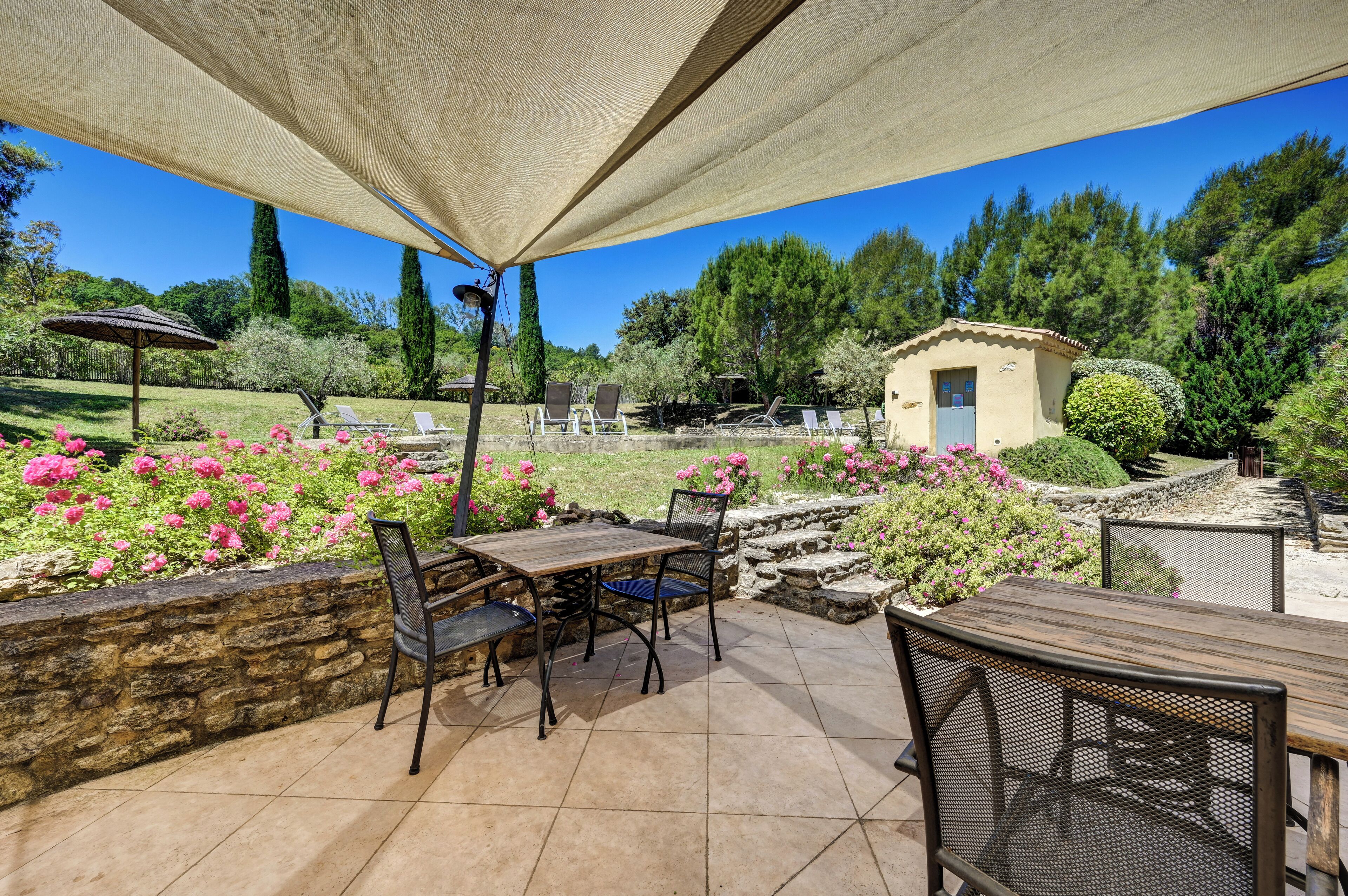 An outdoor patio with a table and chairs, surrounded by a stone wall and flowering plants.