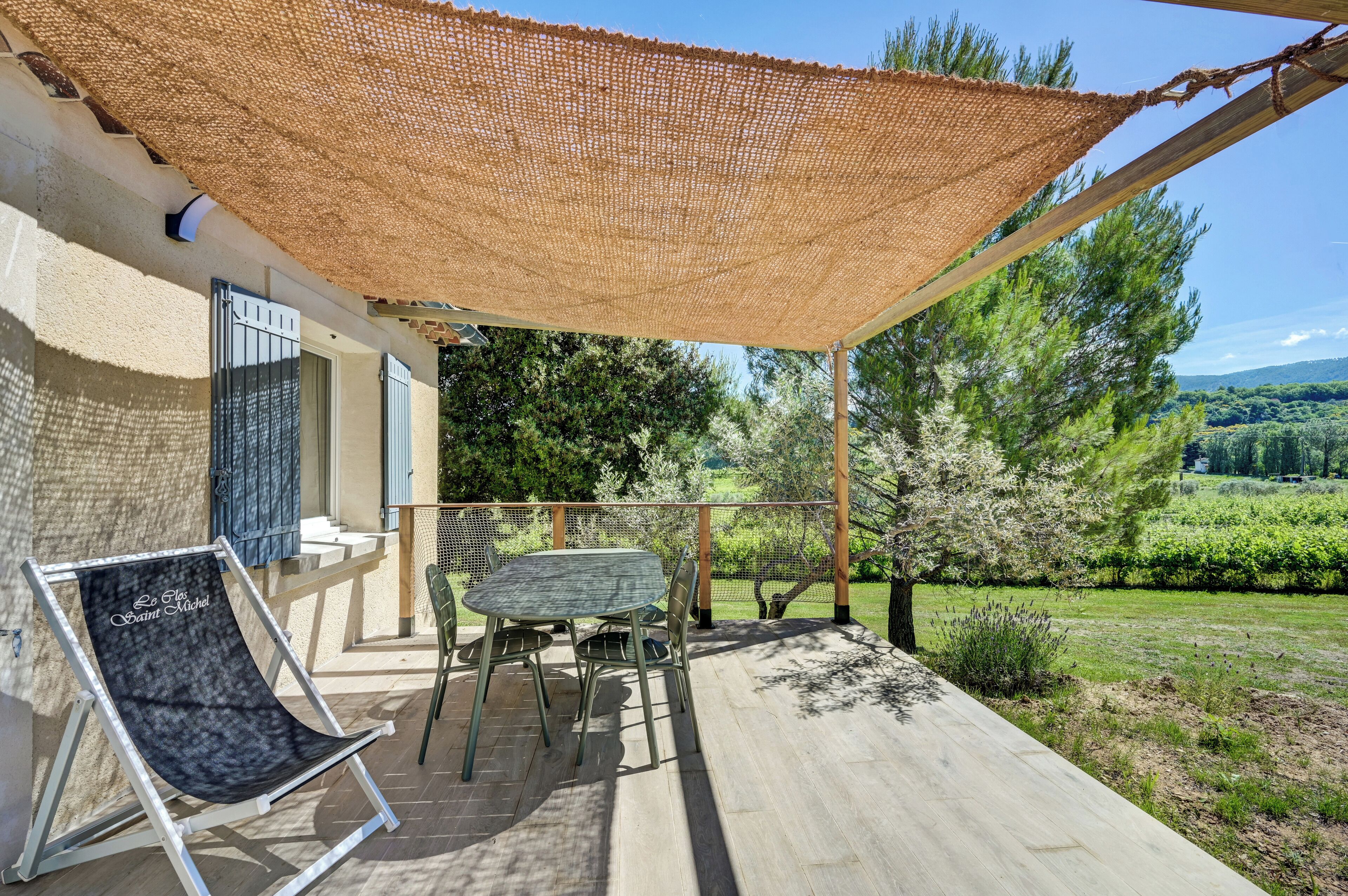 Un espacio al aire libre cubierto con una mesa y sillas, un sillón colgante y vistas a un paisaje verde.