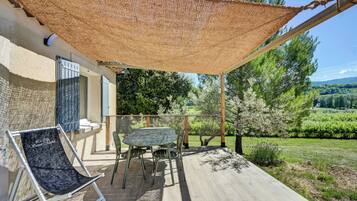 Un espacio al aire libre cubierto con una mesa y sillas, un sillón colgante y vistas a un paisaje verde.