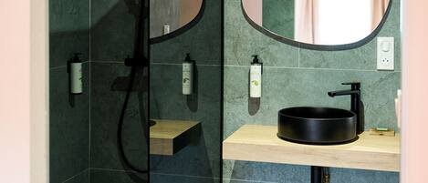 A modern bathroom with a glass shower enclosure, a wooden ceiling, a round mirror, and a black sink.