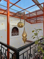 Interior tradicional con un adorno de latón colgante, una estructura de celosía de madera y una pared blanca con rejas decorativas en la ventana.