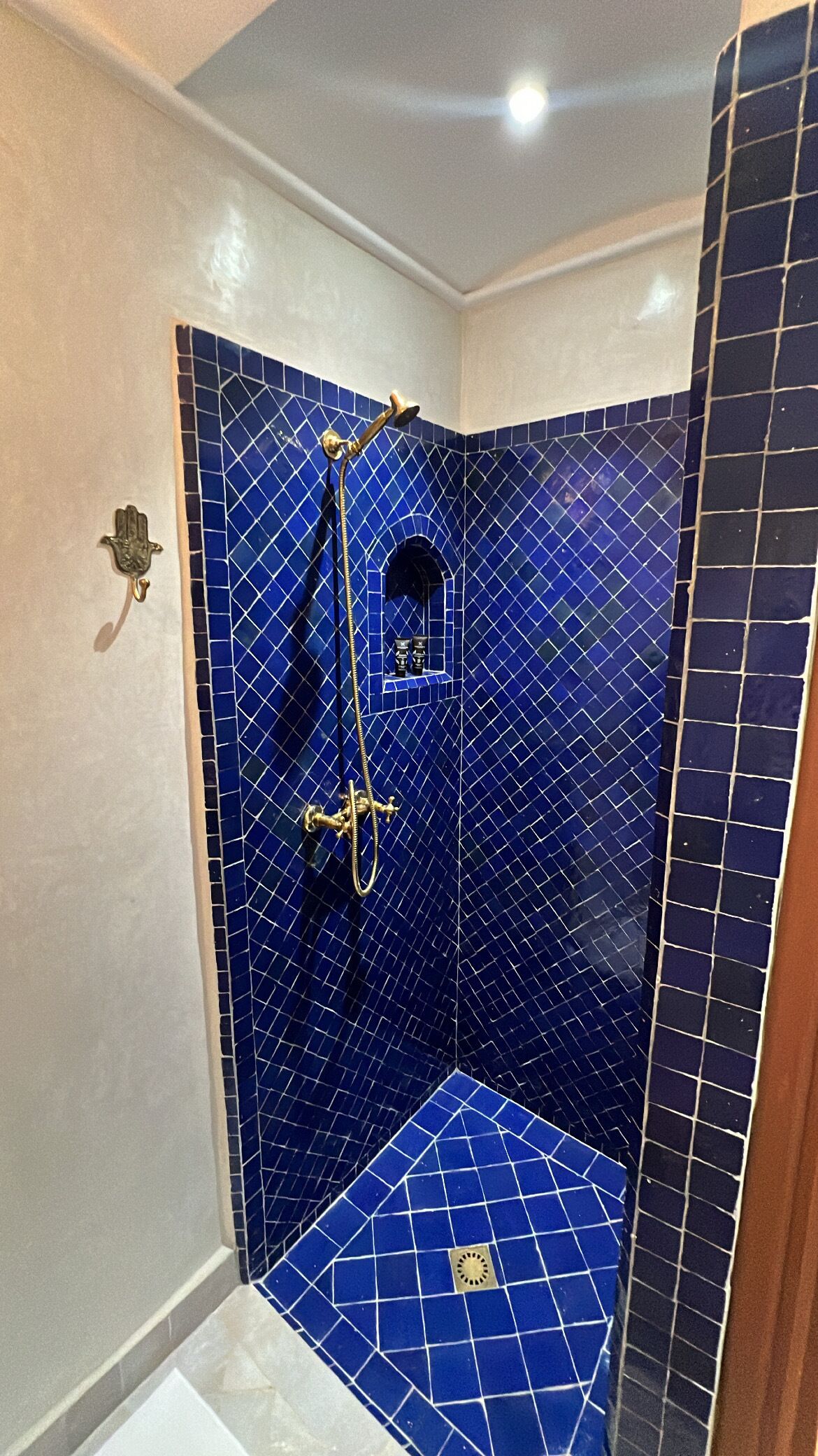 Ein kleines Duschbad mit blauen Fliesen, einer Handbrause und einem Wandarmaturen.