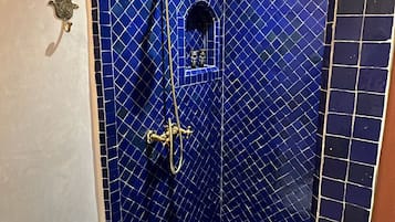 Ein kleines Duschbad mit blauen Fliesen, einer Handbrause und einem Wandarmaturen.