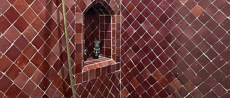 Un área de ducha con pared de azulejos, un cabezal de ducha y un estante con artículos de aseo.
