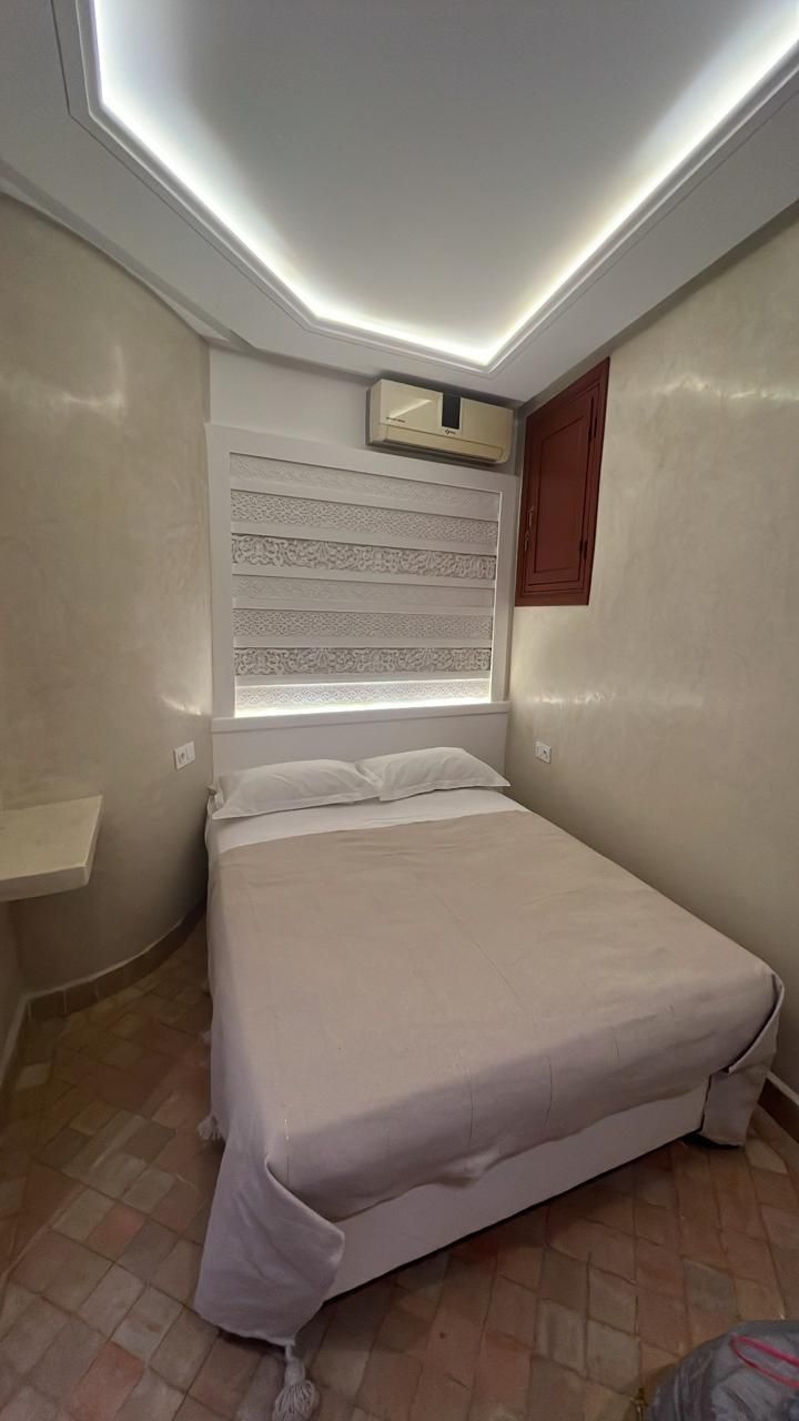 A bedroom with a bed, a window with blinds, a ceiling light, and a wall-mounted air conditioner.