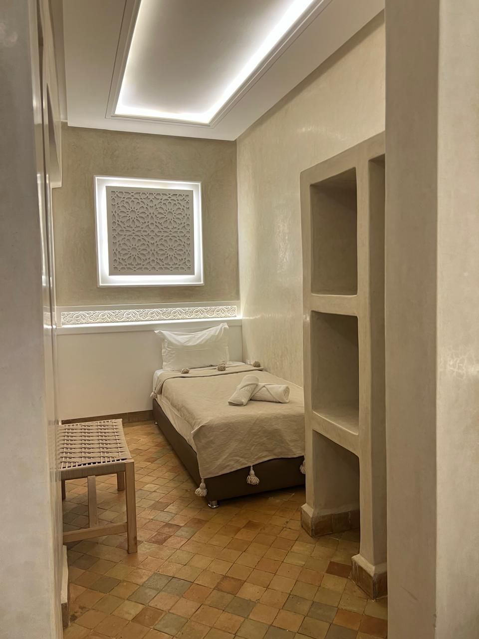 Un dormitorio pequeño y bien iluminado, con una cama, una mesita y un ventanal.