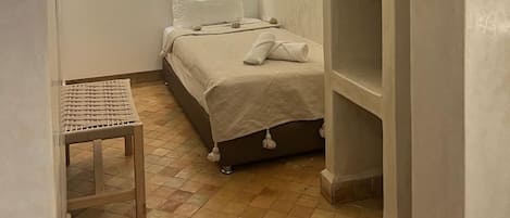A small, well-lit bedroom with a bed, a small table, and a window.