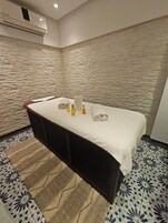 Un cuarto de spa con una camilla de masaje, toallas y botellas de aceites esenciales.