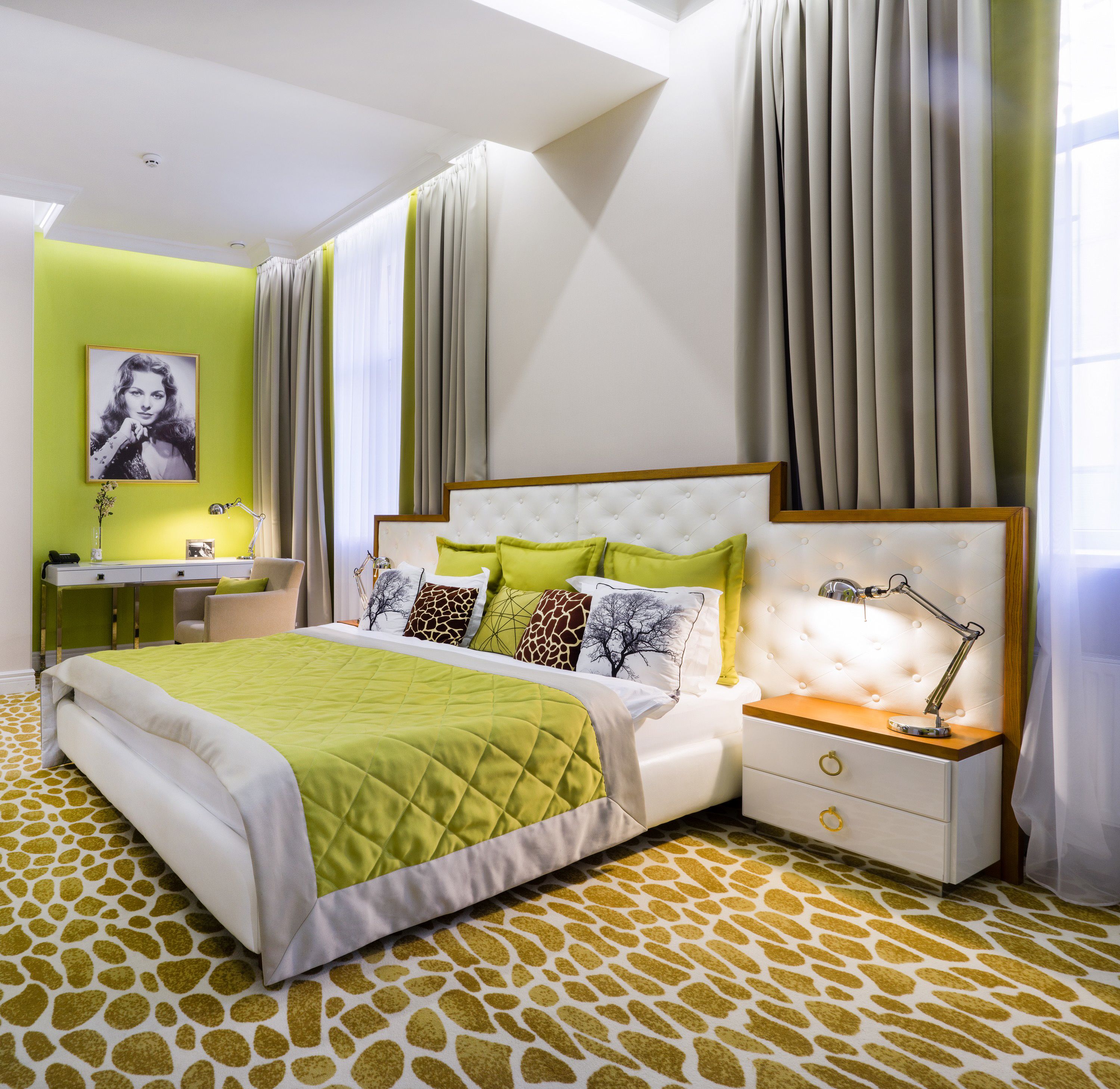 A modern bedroom with a bed, bedside table, lamp, and a desk with a chair.