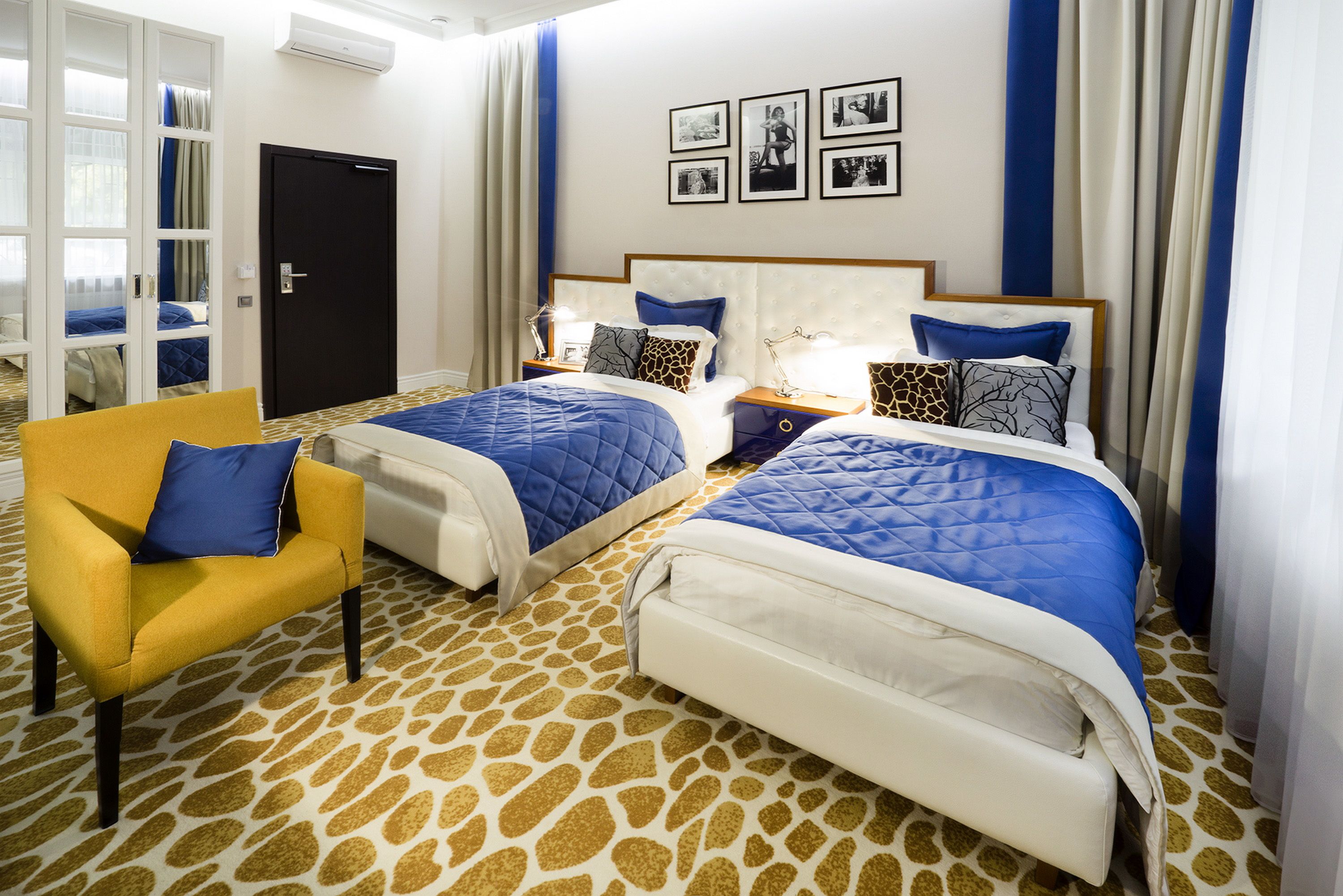 Ein Hotelzimmer mit zwei Betten, einem gelben Sessel und einem gemusterten Teppich.