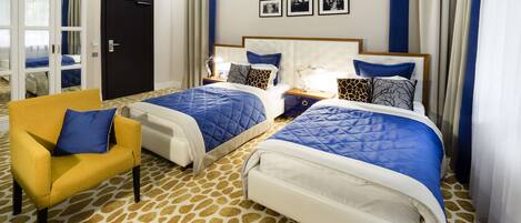 A hotel room with two beds, a yellow armchair, and a patterned carpet.