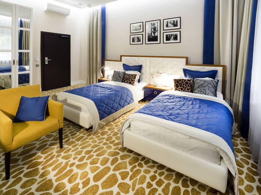 A hotel room with two beds, a yellow armchair, and a patterned carpet.