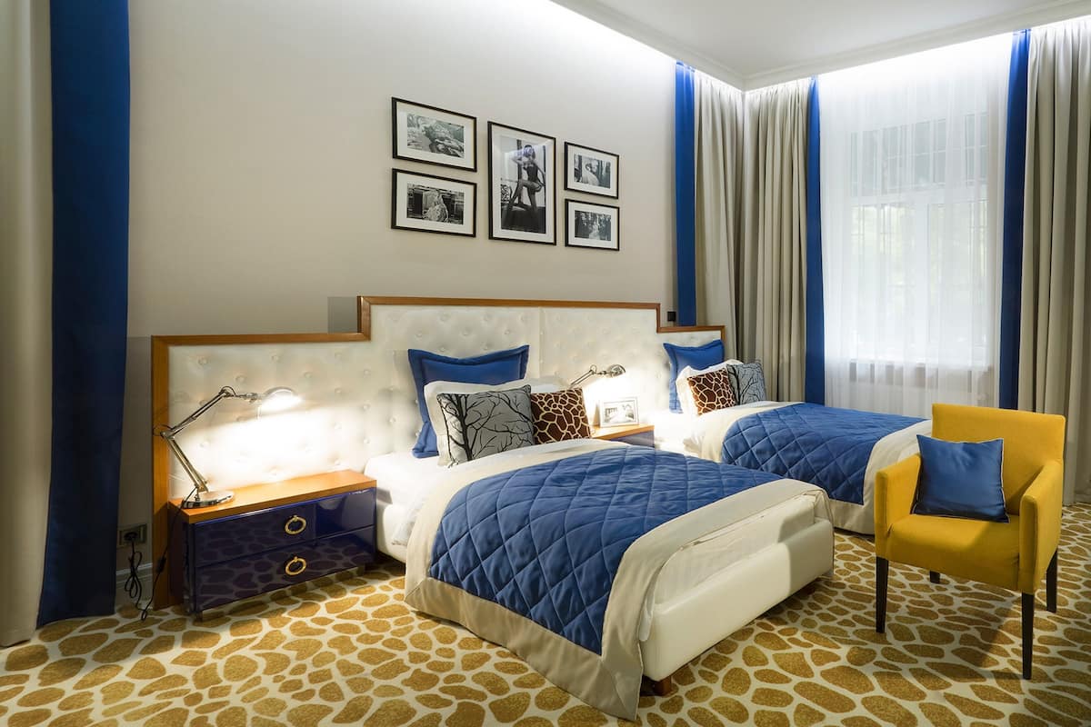 Een hotelkamer met twee bedden, een nachtkastje met lamp, een stoel en een kamerbreed tapijt met een patroon.