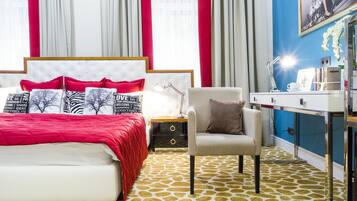 A bedroom with a bed, nightstand, chair, desk, and a large window with curtains.