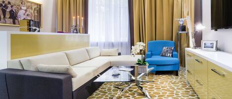Una sala de estar moderna con un sofá seccional, una mesa de centro de vidrio, un sillón azul y una alfombra estampada.