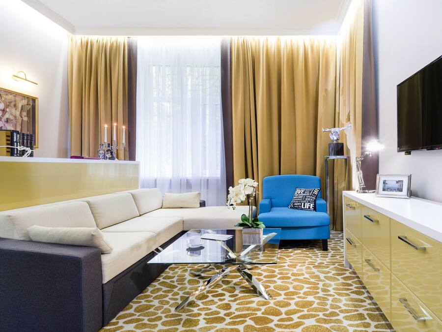 Una sala de estar moderna con un sofá seccional, una mesa de centro de vidrio, un sillón azul y una alfombra estampada.