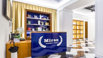 A reception desk with a blue sign reading "Mirax boutique hotel" and a wooden shelf with various items.