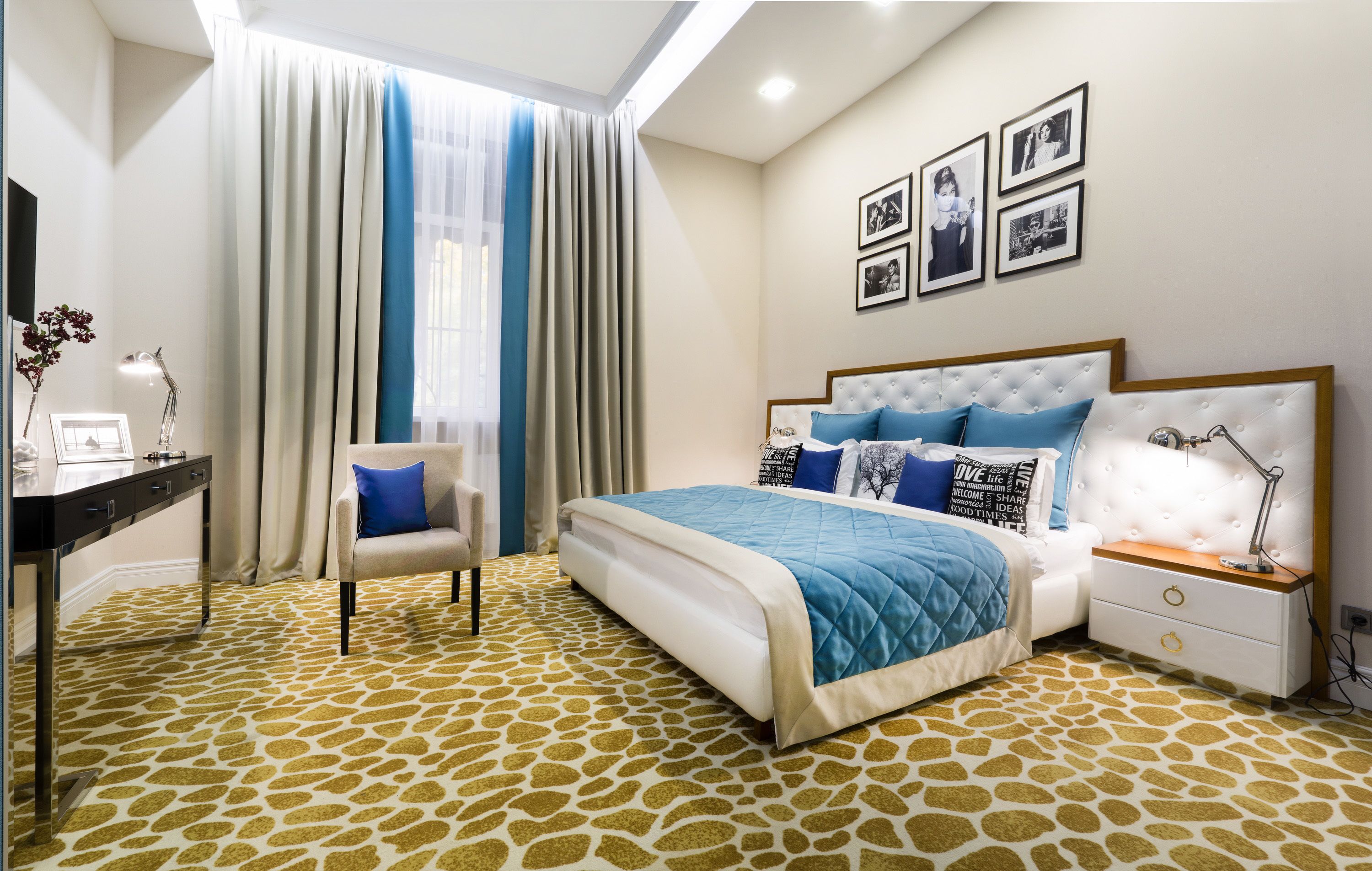 A bedroom with a bed, a chair, a desk, and a nightstand.