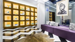 Un intérieur moderne avec un sol à motifs, un canapé violet agrémenté de coussins décoratifs et un mur composé d’étagères illuminées où sont exposés divers objets.