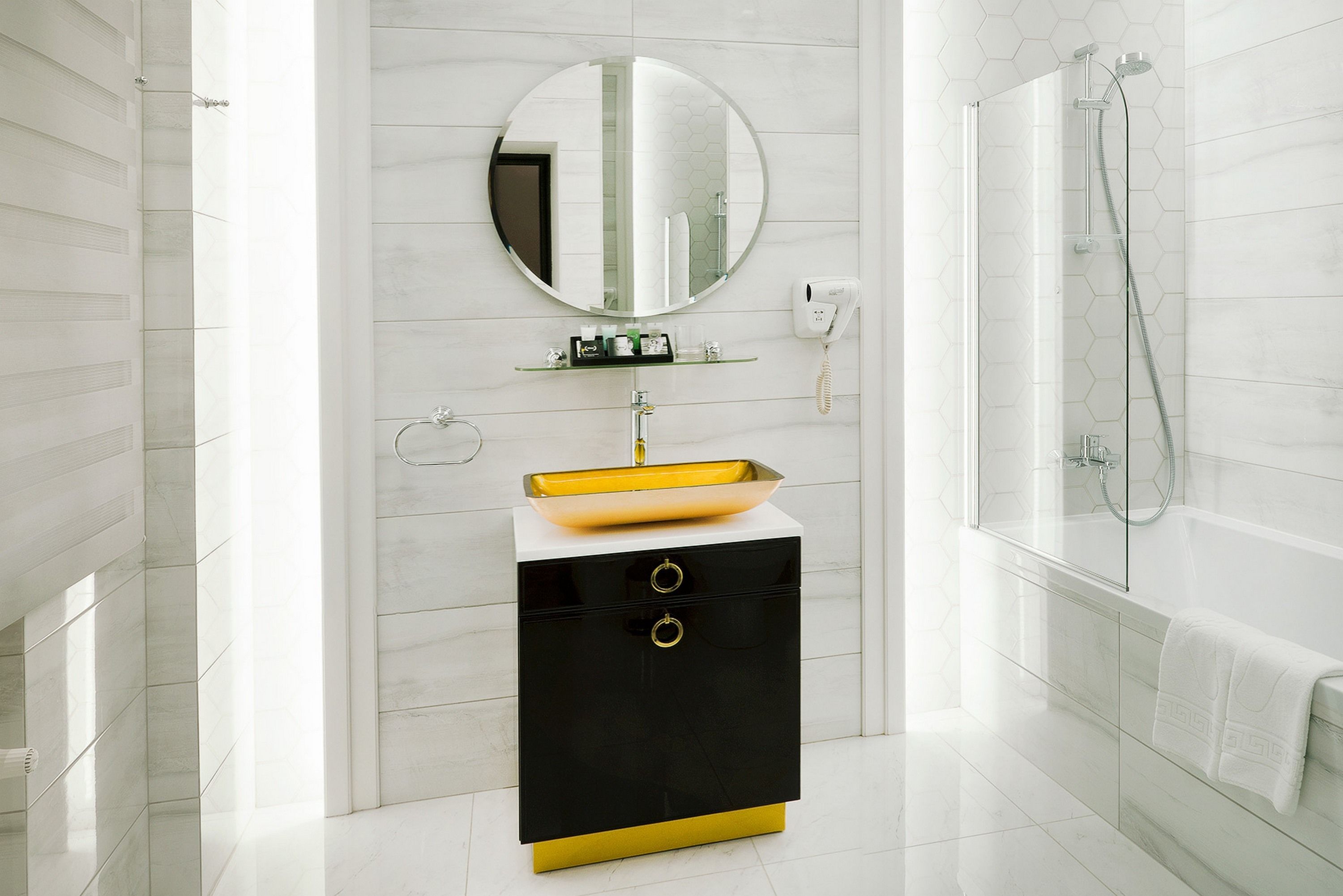 A modern bathroom with a white and black vanity, a round mirror, a yellow sink, and a glass-enclosed shower.