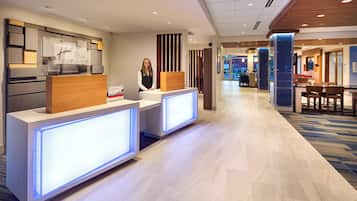 A hotel reception area with a modern design, featuring a reception desk, a waiting area, and a visible staircase leading to other floors.