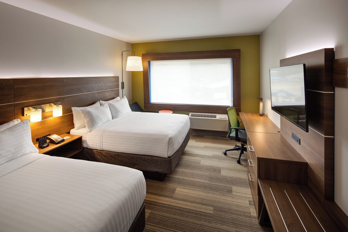 Habitación de hotel con dos camas, un escritorio, una silla, un televisor y una ventana con persianas.