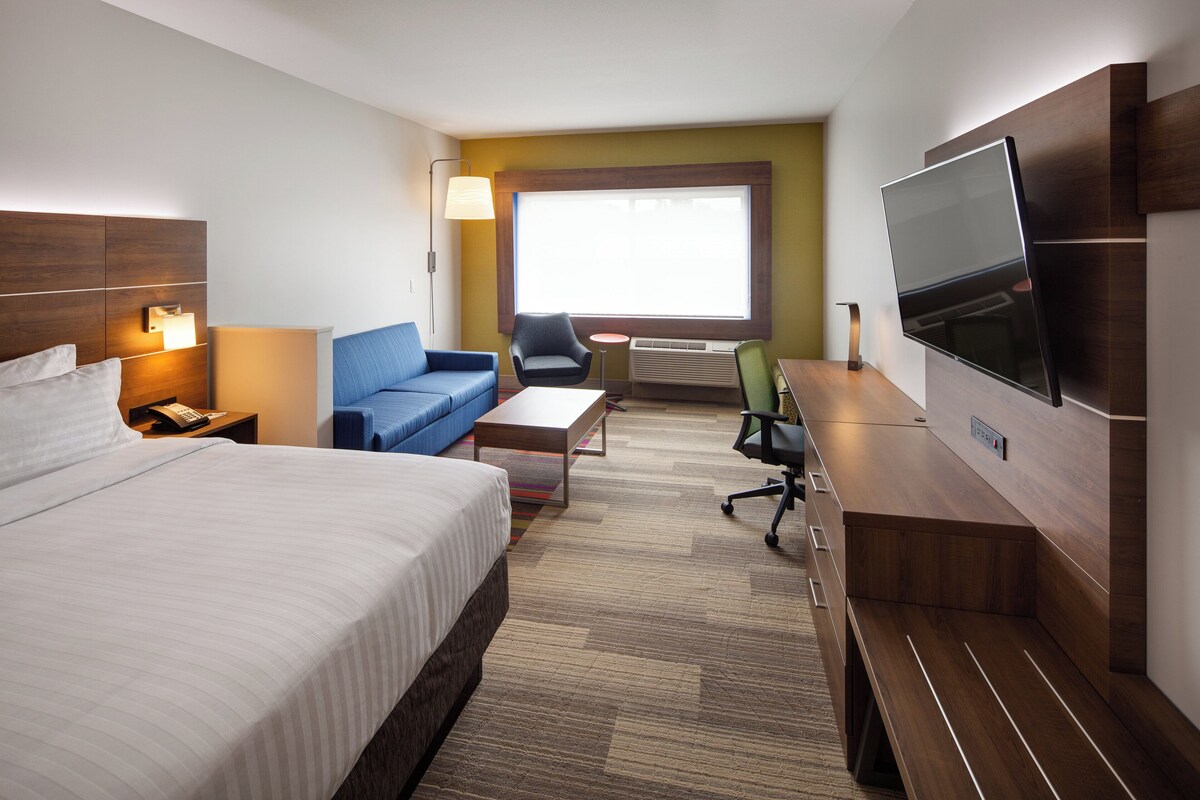 Habitación de hotel con cama, sofá, escritorio, silla, televisión y ventana.