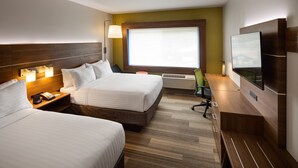 Ein Hotelzimmer mit zwei Betten, einem Schreibtisch, einem Stuhl, einem Fernseher und einem Fenster mit Jalousien.