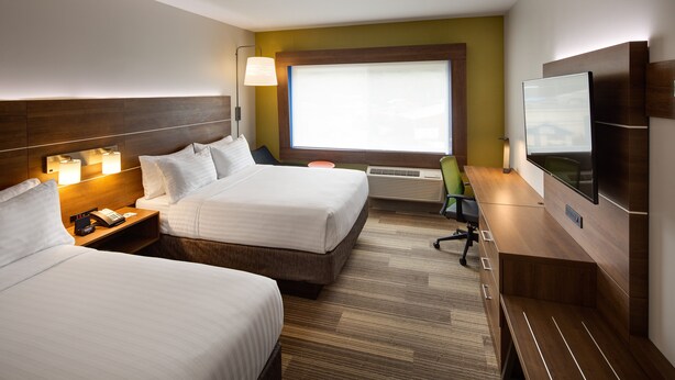 A hotel room with two beds, a desk, a chair, a TV, and a window with blinds.
