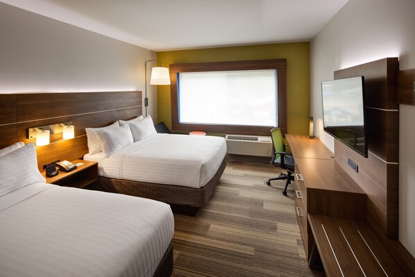 Een hotelkamer met twee bedden, een bureau, een stoel, een televisie en een raam met zonwering.