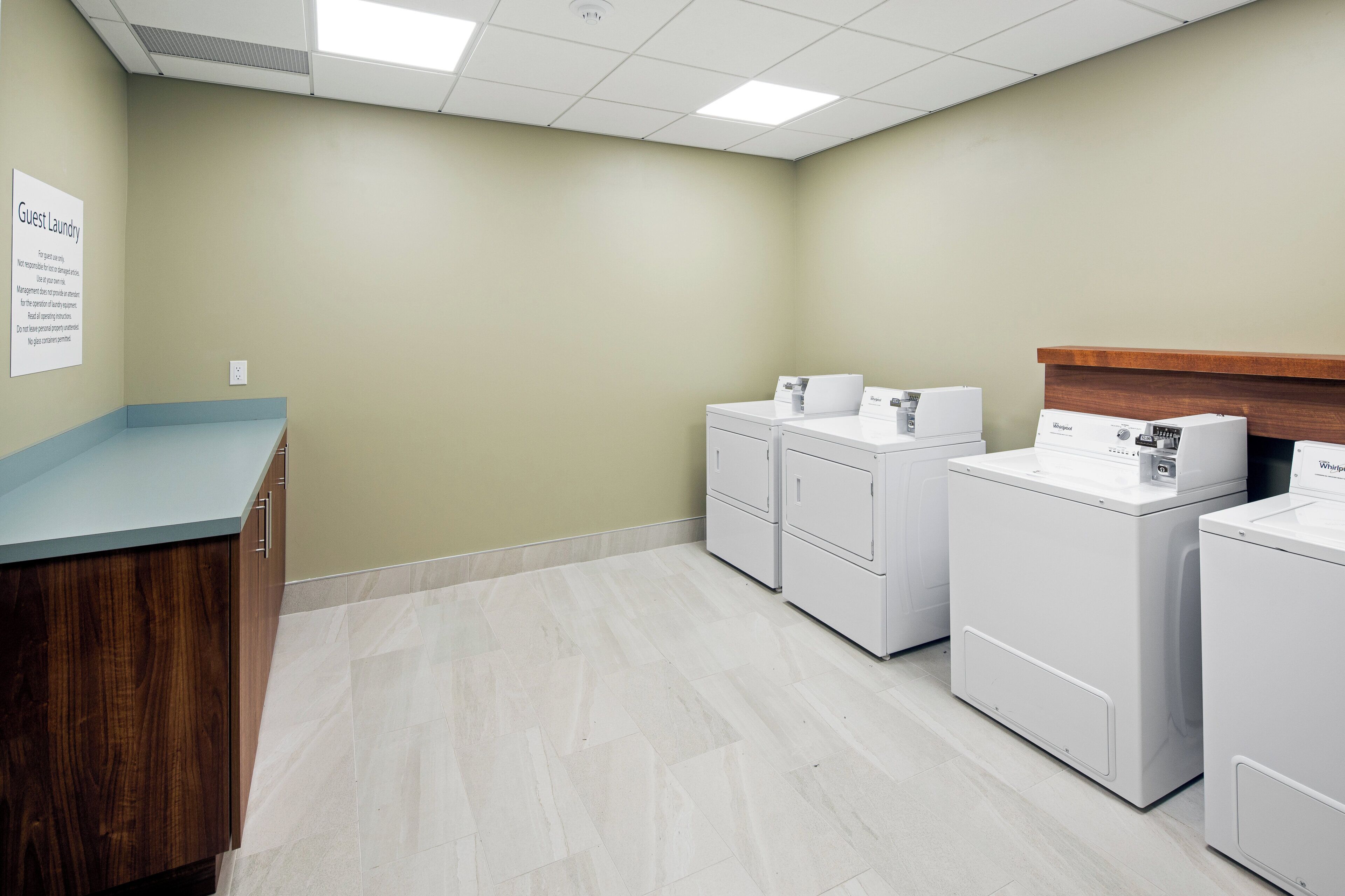 A laundry facility with a counter, multiple washing machines, and a sign indicating guest laundry use.