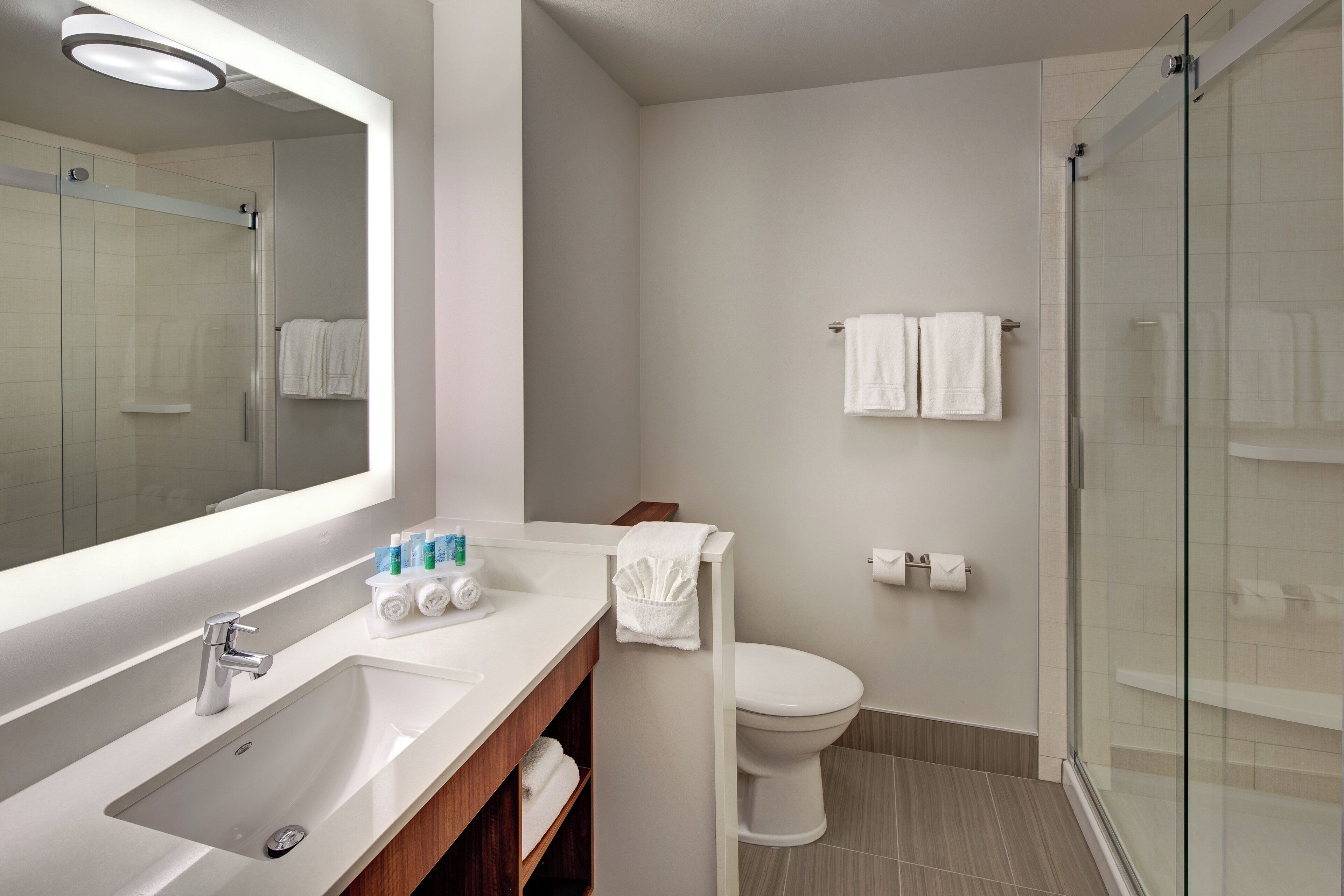 Un baño moderno con lavamanos, espejo, inodoro y cabina de ducha de vidrio.