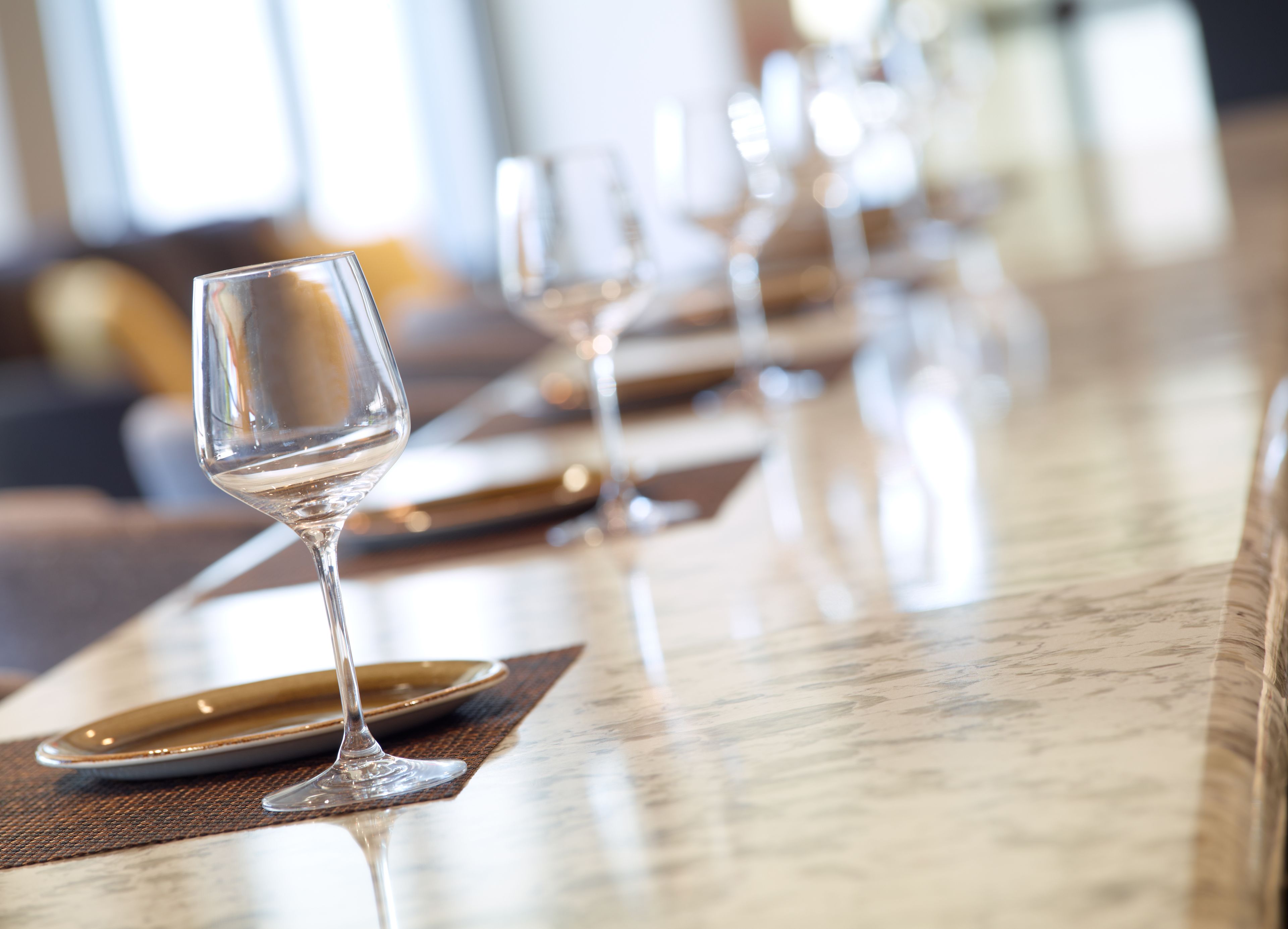 A row of empty wine glasses on a marble bar counter with placemats and plates.