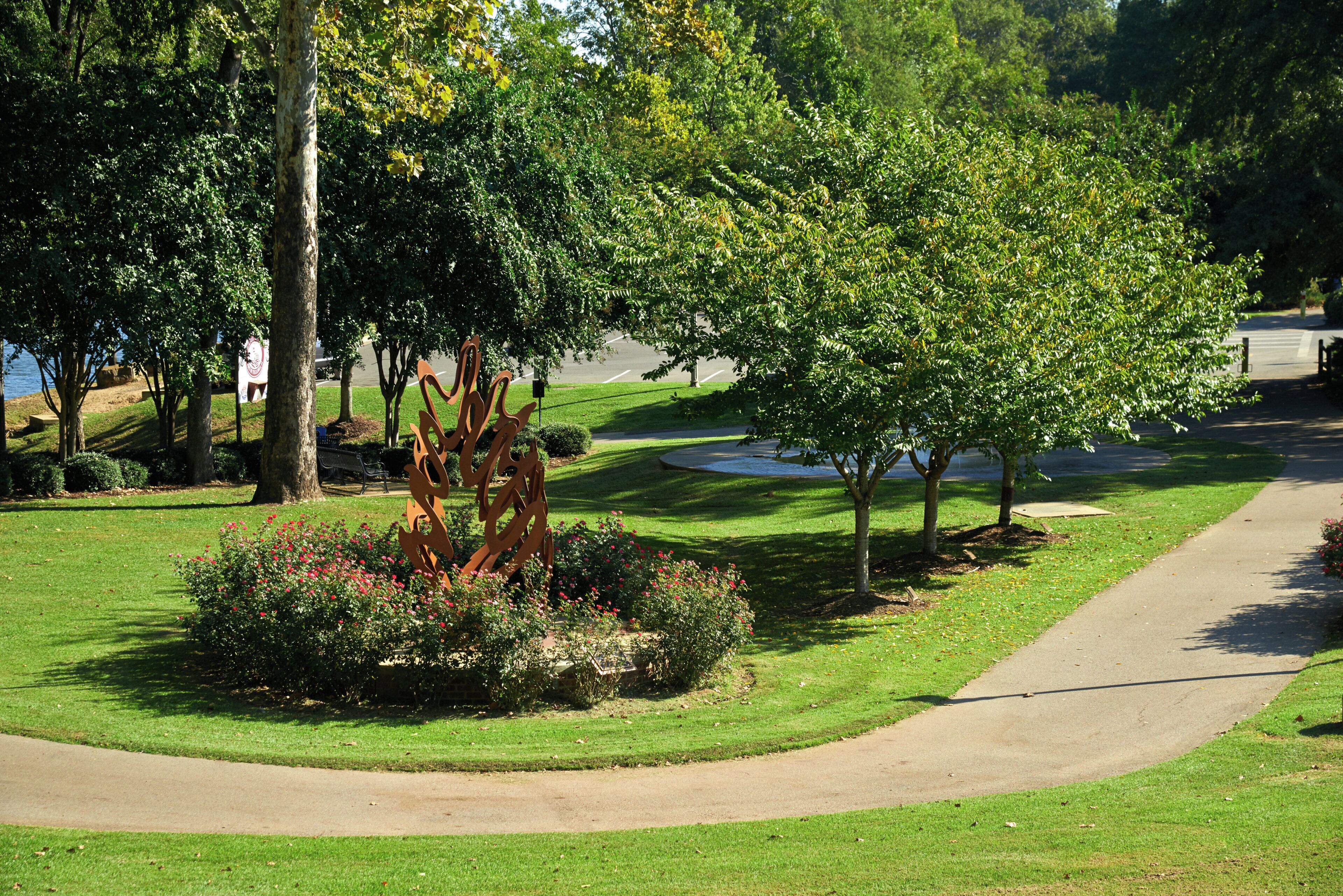 A park with a paved walkway, trees, and a sculpture.