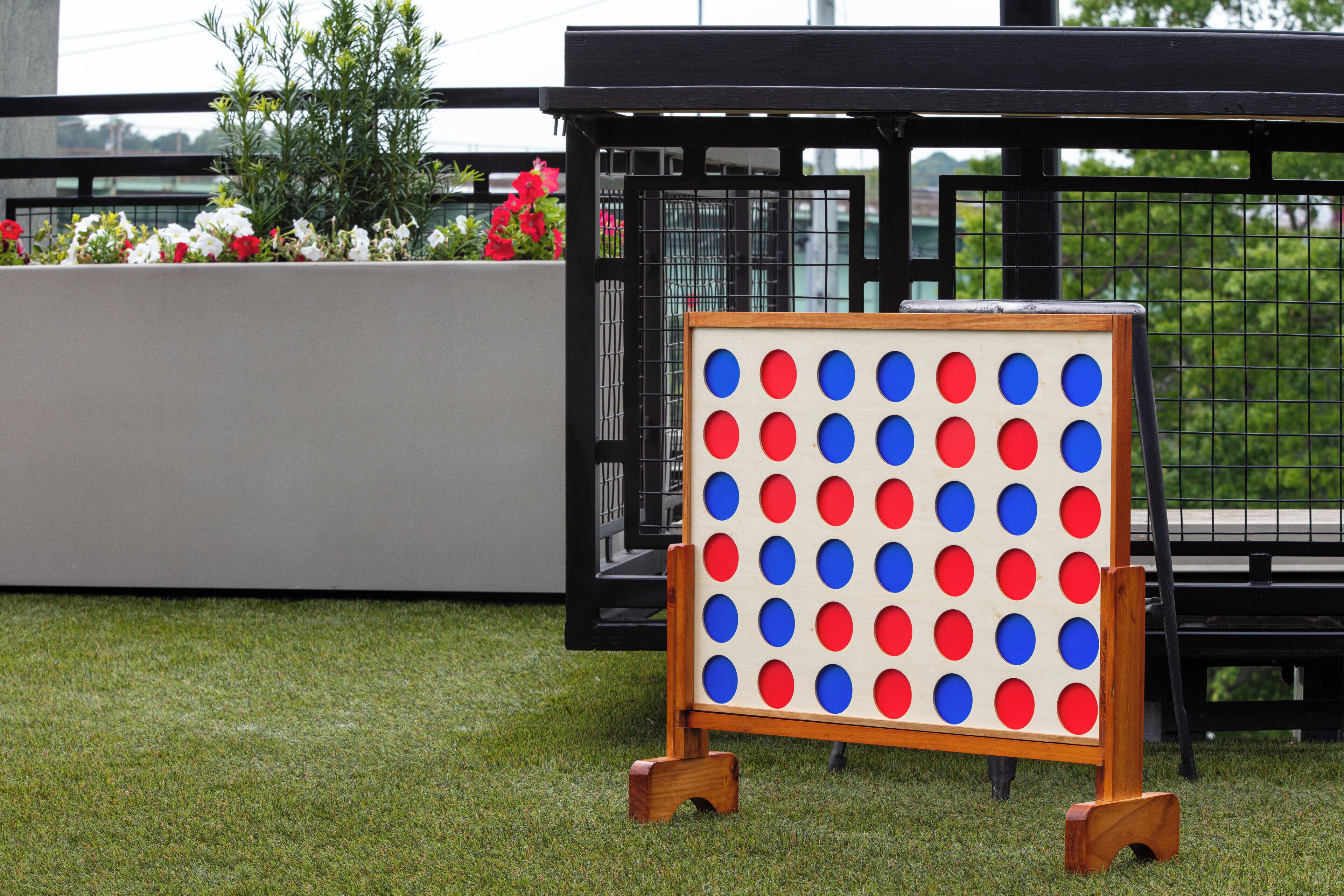 A tic-tac-toe board on a grassy area with a metal fence and flowers in the background.