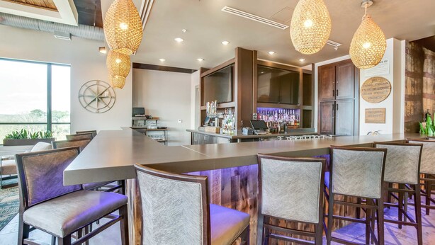 A modern bar area with a long counter, multiple hanging light fixtures, and a bar stocked with bottles. - Hotel Indigo Tuscaloosa Downtown by IHG (Tuscaloosa)