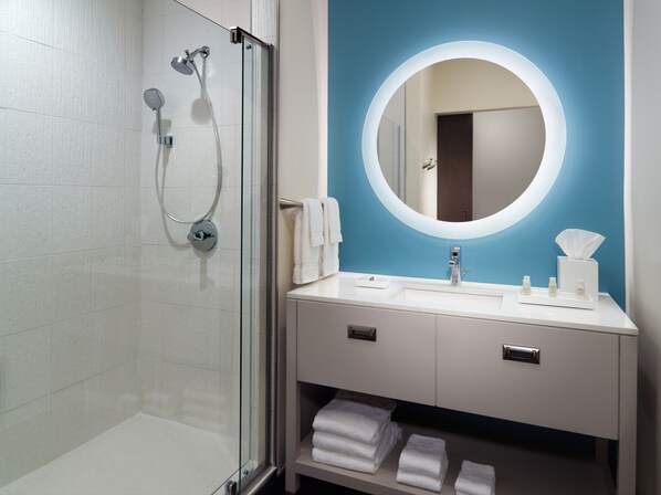 Un baño moderno con ducha envuelta en vidrio, un espejo redondo y un tocador blanco con una pared de acento azul.