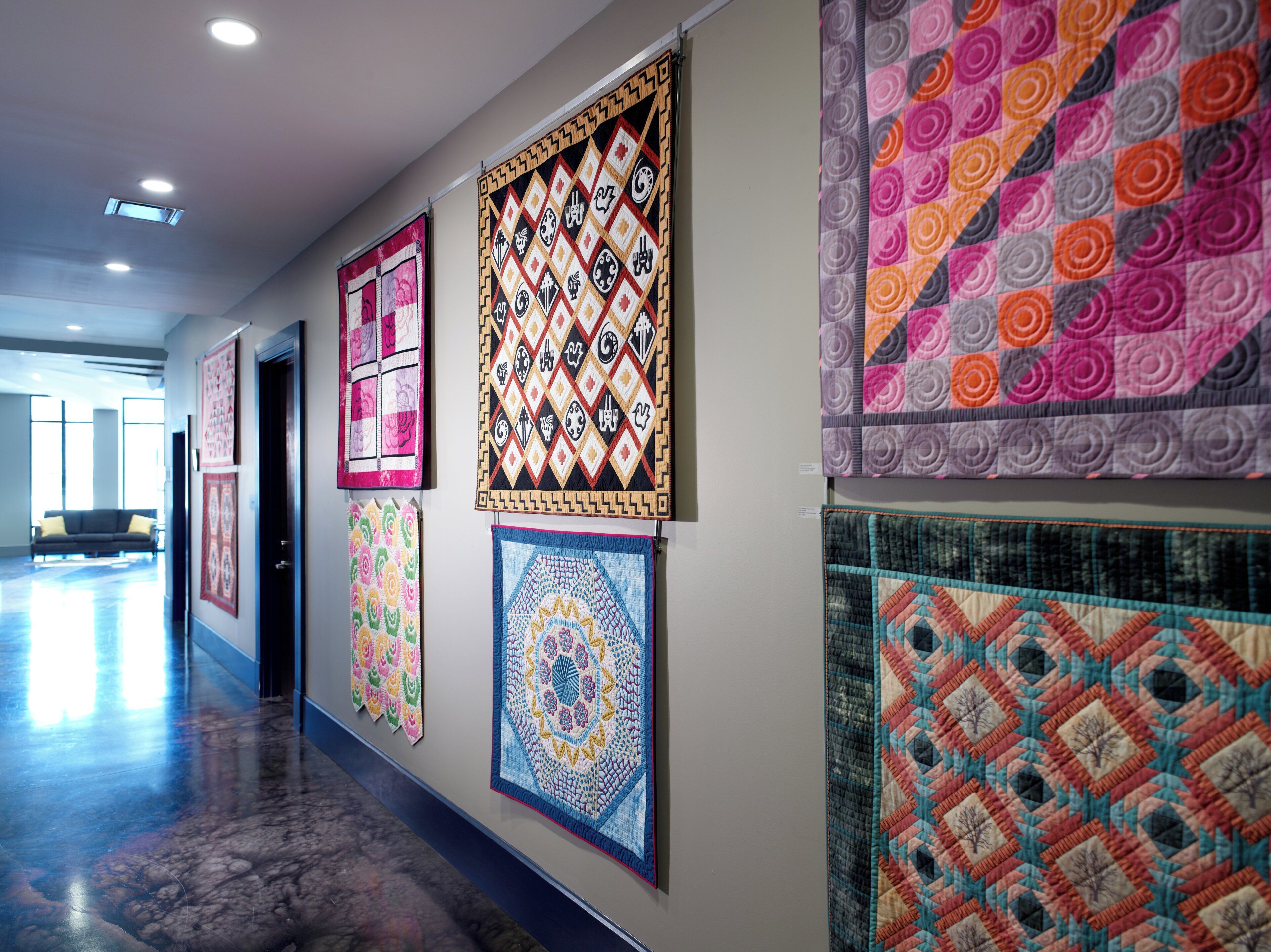 A hallway with multiple quilts displayed on the wall, a sofa, and a door.