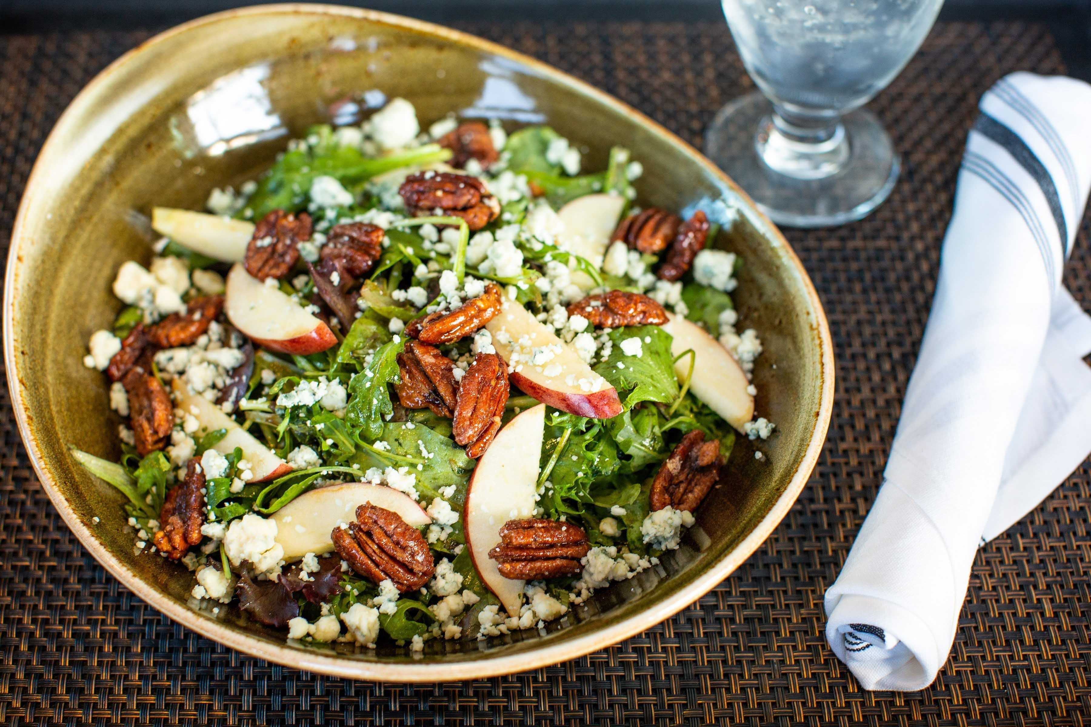 A bowl of salad with pecans and cheese on a woven placemat.