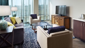 A modern hotel room with a sofa, armchair, coffee table, and a TV on a wooden cabinet. - Hotel Indigo Tuscaloosa Downtown by IHG (Tuscaloosa)