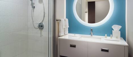 Ein modernes Badezimmer mit einer gläsernen Duschkabine, einem runden Spiegel und einem weißen Waschtisch mit blauer Akzentwand.