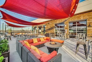 An outdoor seating area with a wicker sofa, round tables, and string lights.